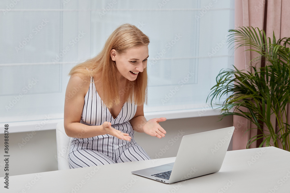 Smiling beautiful blonde girl sitting at home and looking at the laptop screen. Smiling beautiful blonde girl sitting at home and looking at the laptop screen.
