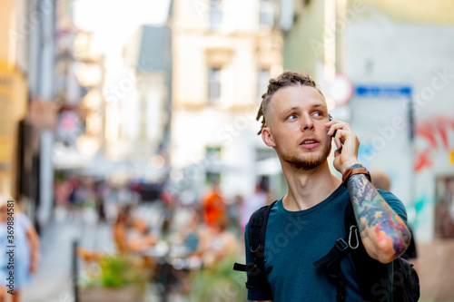 young guy with dreadlocks is talking on the phone on city street