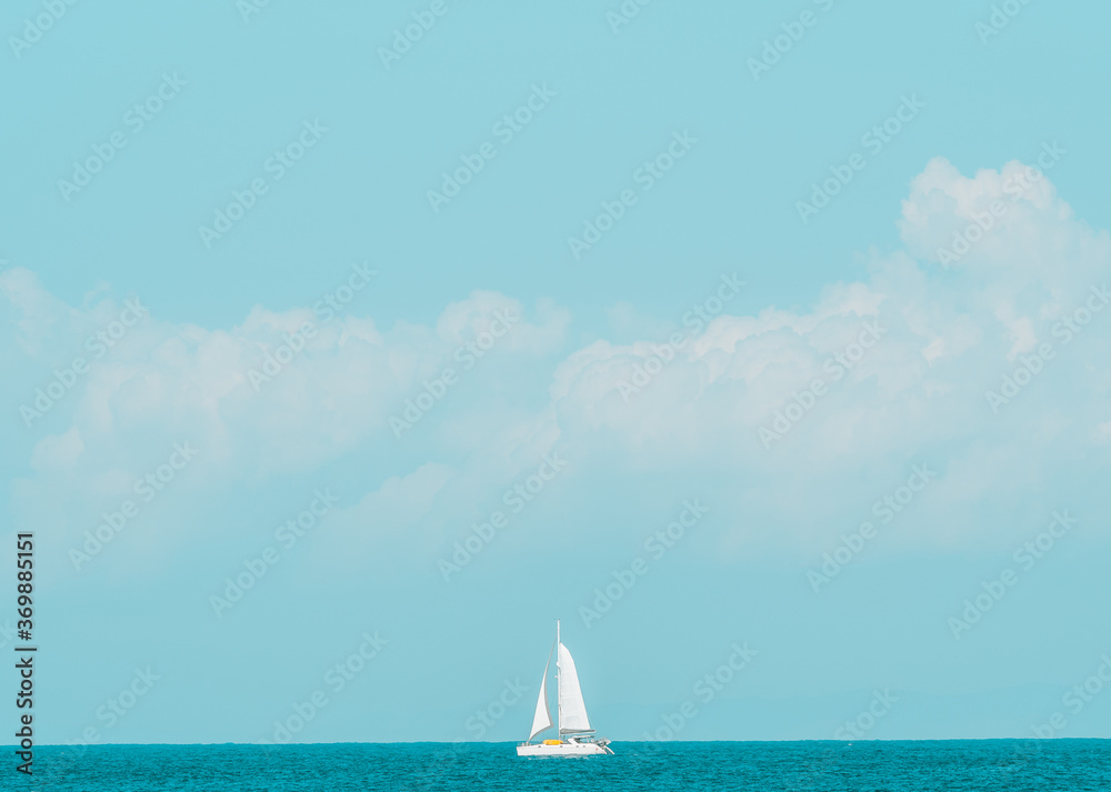 Sailing boat on the horizon in front of fluffy clouds and blue sky