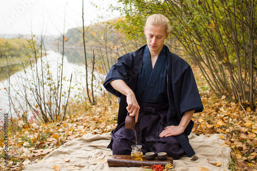 Man in traditional japanese clothes making tea in autumn park