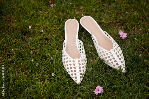 White leather middle heel female sandals standing on the grass. Sakura flowers. 