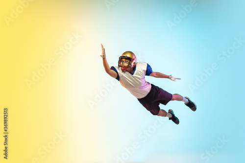 Catching. American football player isolated on gradient studio background in neon light. Professional sportsman during game playing in action and motion. Concept of sport, movement, achievements.