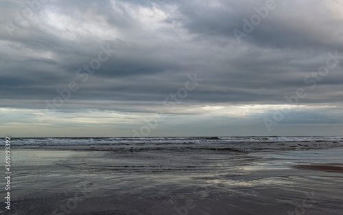 Fototapeta Naklejka Na Ścianę i Meble -  A line of Surf coming in to the Beach at St Cyrus under heavy clouds from a Summer Storm, with small ripples of water coming up the beach.