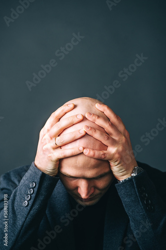 Frustrated bald man holding his head facing camera. Isolated on dark background