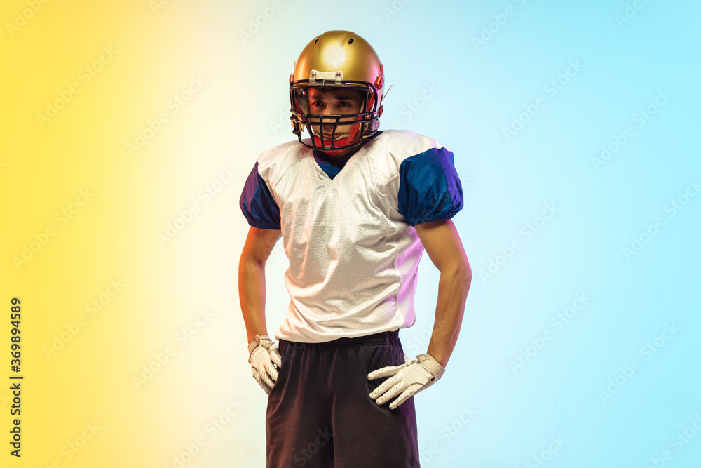 American football player isolated on gradient studio background in neon light. Professional sportsman posing confident and strong during game playing. Concept of sport, movement, achievements.