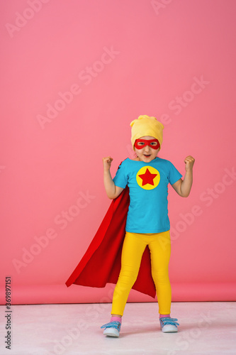 little girl in a superhero costume in red Cape and hat shows how strong she is.