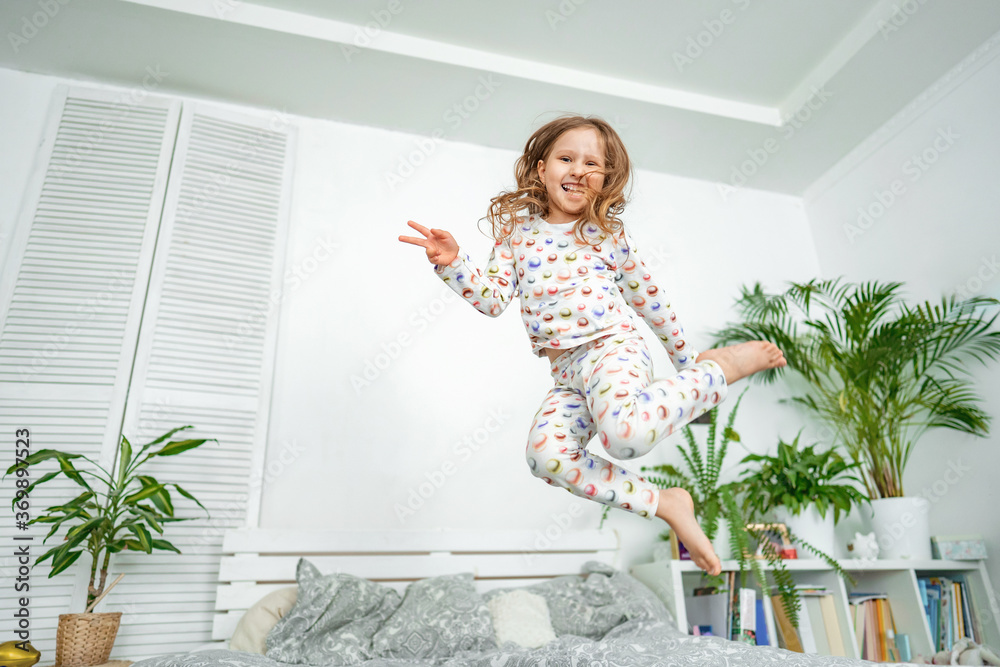 happy little girl jumps in her pajamas on bed in morning after night's sleep. happy little girl jumps in her pajamas on bed in morning after night's sleep.