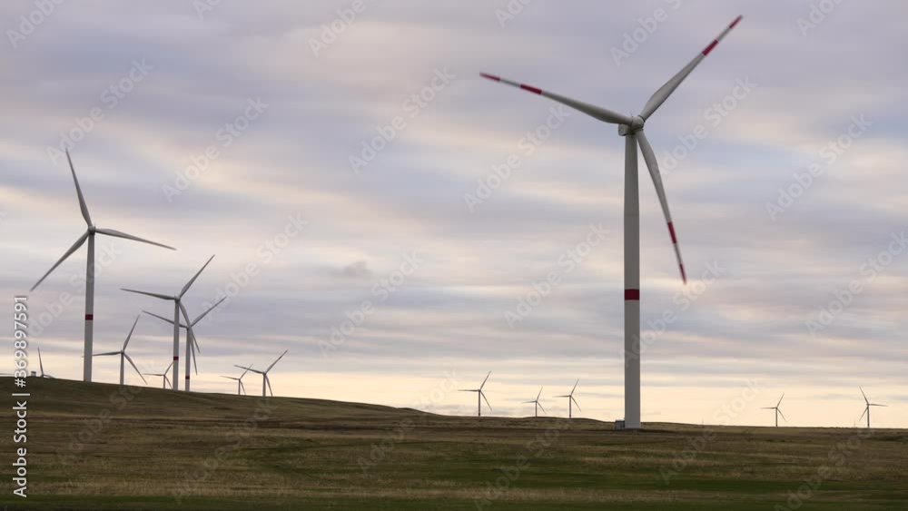Motion the blades of a large wind turbine in a field against a background of orange sunset on the horizon with a beautiful hills. Alternative energy sources. Windy park. Ecological energy.Industrial Motion the blades of a large wind turbine in a field against a background of orange sunset on the horizon with a beautiful hills. Alternative energy sources. Windy park. Ecological energy.Industrial