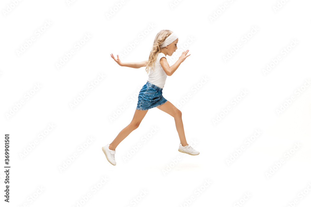 On the way. Happy kids, little and emotional caucasian girl jumping and running isolated on white background. Look happy, cheerful, sincere. Copyspace for ad. Childhood, education, happiness concept.