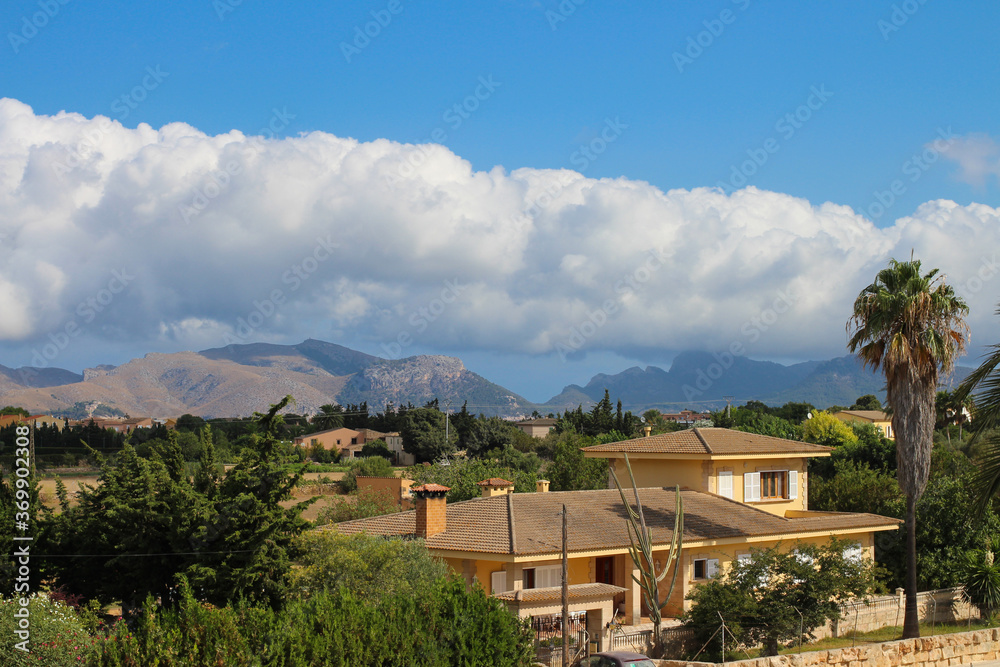 one of the houses in the city of Alcudia against the blue sky with clouds and mountains. Alcudia. Majorca. Spain.
