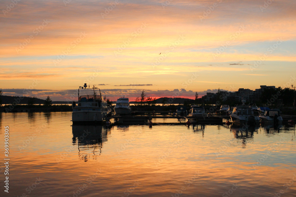 White boats and yachts moored to the pier, reflected in the water of lake Vesijarvi at sunset. Lahti. Finland.