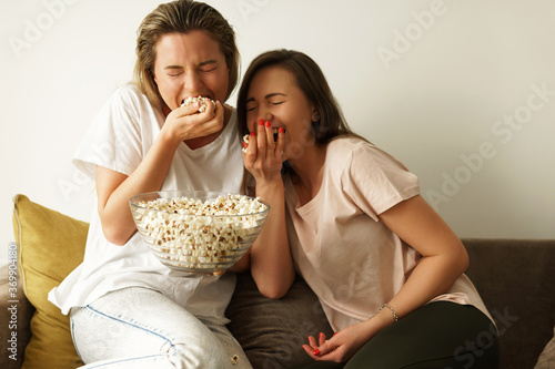 Two beautiful girlfriends watching tv show and eating popcorn