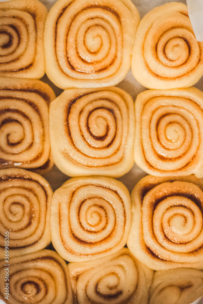 Delicious homemade raw cinnamon rolls bun dough in the rectangle shaped baking tray on the white baking paper. Top view.