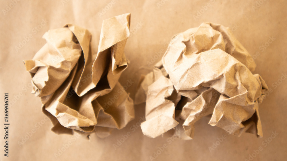 A wrinkled brown paper ball crumpled on a brown background A wrinkled brown paper ball crumpled on a brown background