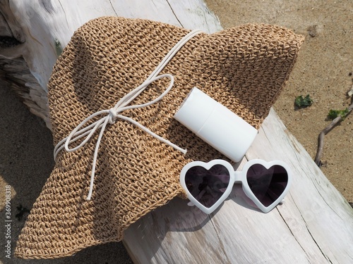 ビーチの必需品、流木の上に置かれたストローハットとサングラスと日焼け止め