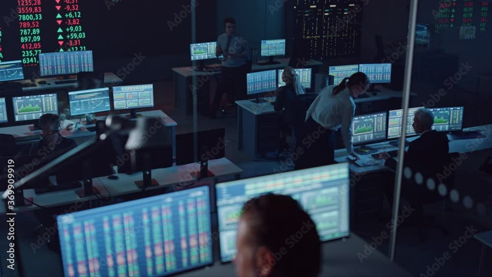 Professional Financial Data Analysts Working in a Modern Monitoring Office with Live Analytics Feed on a Big Digital Screen. Monitoring Room with Finance Specialists Sit in Front of Computers. 