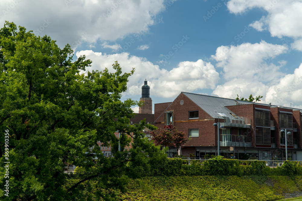 A modern building with balconies, behind it an old water tower. Beautiful blue sky with white clouds in the background. There is green grass and trees underneath the building.