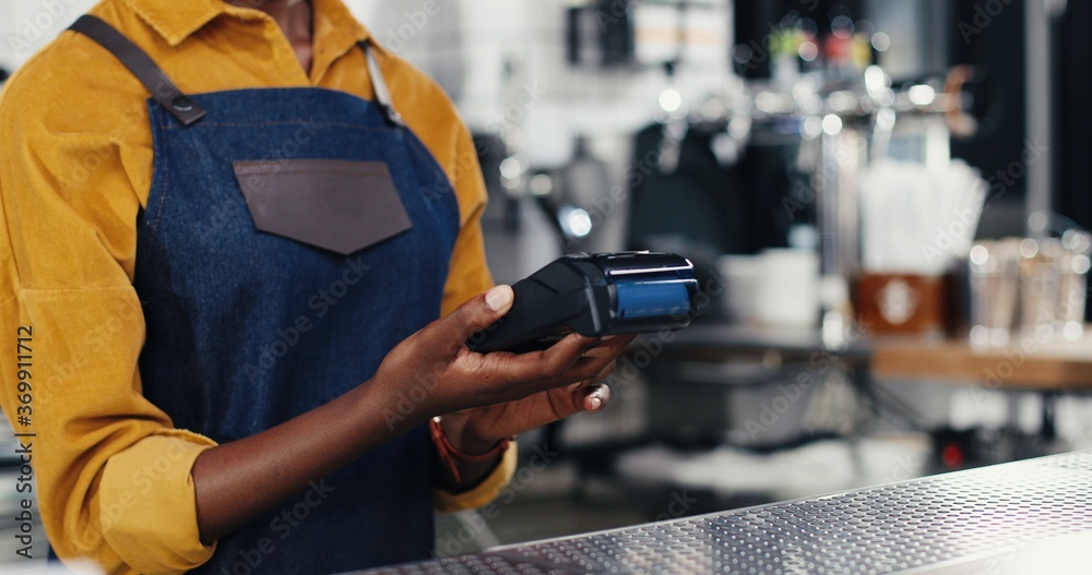 Close up hands of multiethnic bartender woman and client man. Caucasian male paying with paypass, credit card. Mixed-races. Passing payment at counter. Pay for drink or food. African American waitress