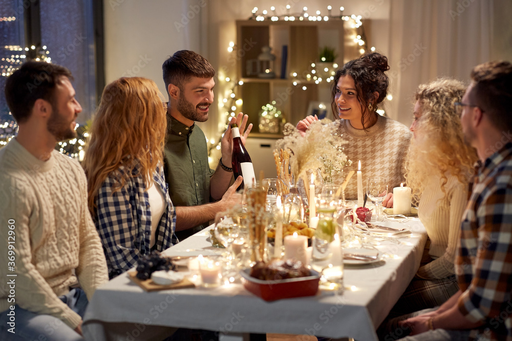 holidays and celebration concept - happy friends having christmas dinner at home with bottle of non-alcoholic red wine