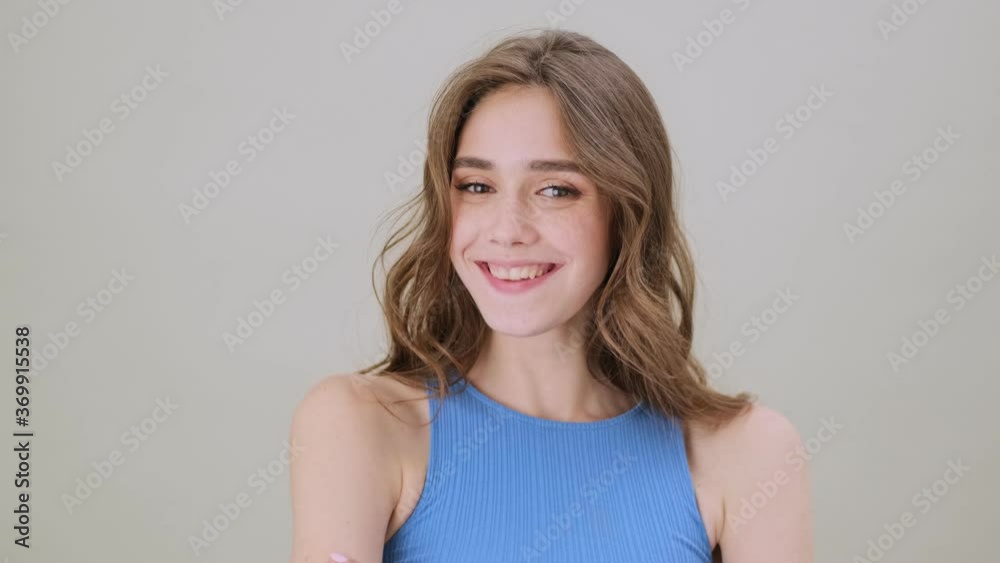 A happy young woman is smiling to the camera standing isolated over gray background in studio A happy young woman is smiling to the camera standing isolated over gray background in studio