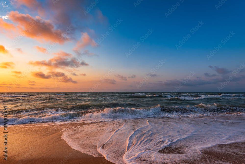 Colorful sunset with wave splashes on the beach