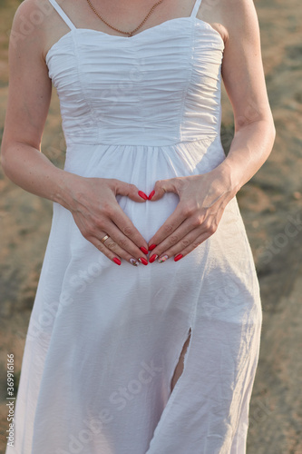 Pregnant girl holds hands on her stomach with heart symbol