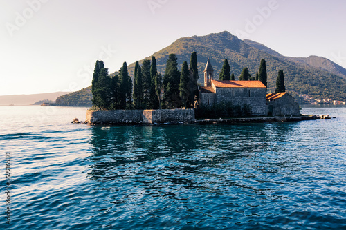 Obraz na płótnie Catholic red roof medieval monastery, bell tower, masonry wall and cypress trees on an island in the Adriatic Sea. Little island in blue water of Kotor bay among Montenegro mountains. Island panorama w salonie