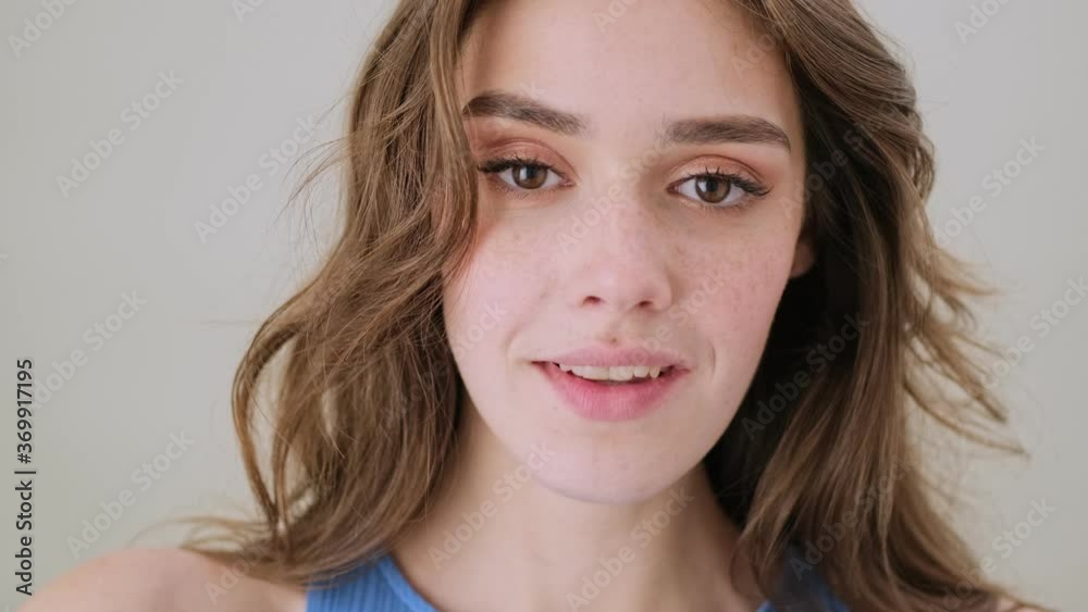 A beautiful young woman is opening her eyes and smiling to the camera standing isolated over gray background in studio A beautiful young woman is opening her eyes and smiling to the camera standing isolated over gray background in studio