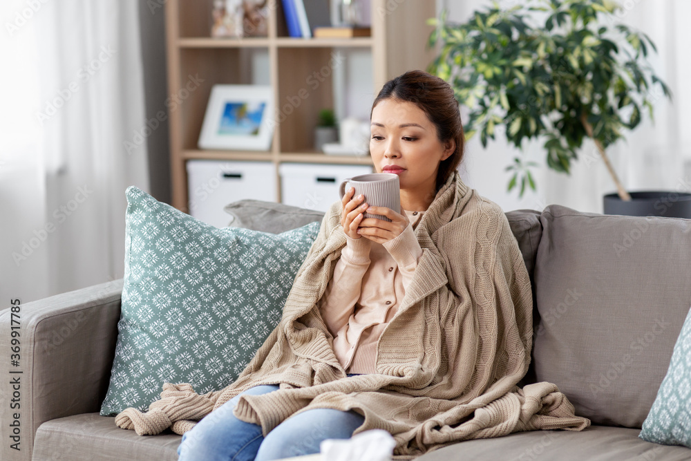 health, cold and people concept - sad sick young asian woman in blanket drinking hot tea at home health, cold and people concept - sad sick young asian woman in blanket drinking hot tea at home