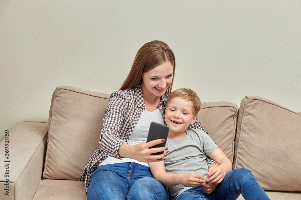 Young beautiful mother communicates online while sitting next to her son.