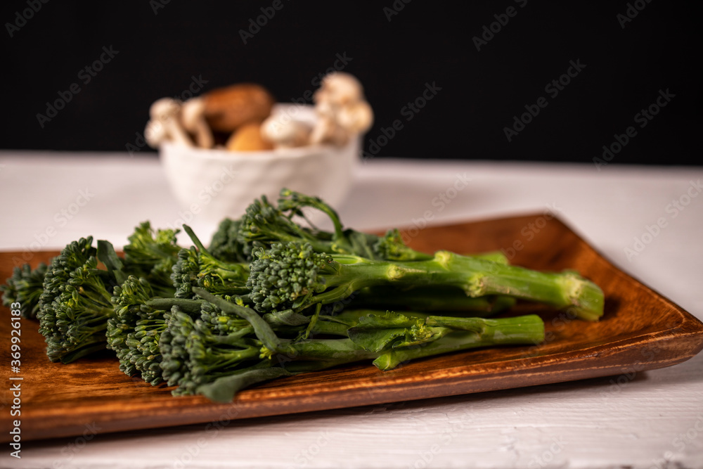 variety of mushrooms on white plate and broccoli on wooden plate for cooking in vegan food variety of mushrooms on white plate and broccoli on wooden plate for cooking in vegan food