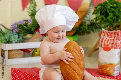 a baby in a cook's hat sits back in a beautiful photo zone with flour and vegetables, a cook's child, a child with flour and bread prepares food