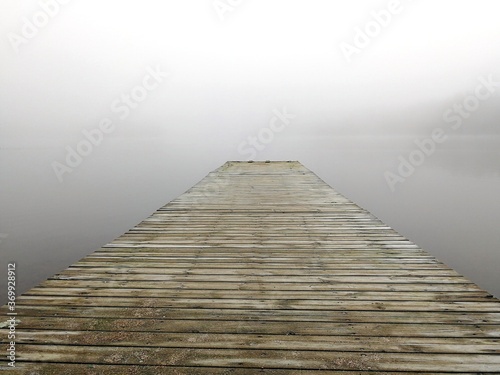 Mystical foggy morning on the lake in autumn. Landscape with a pier against the backdrop of a vanishing horizon.