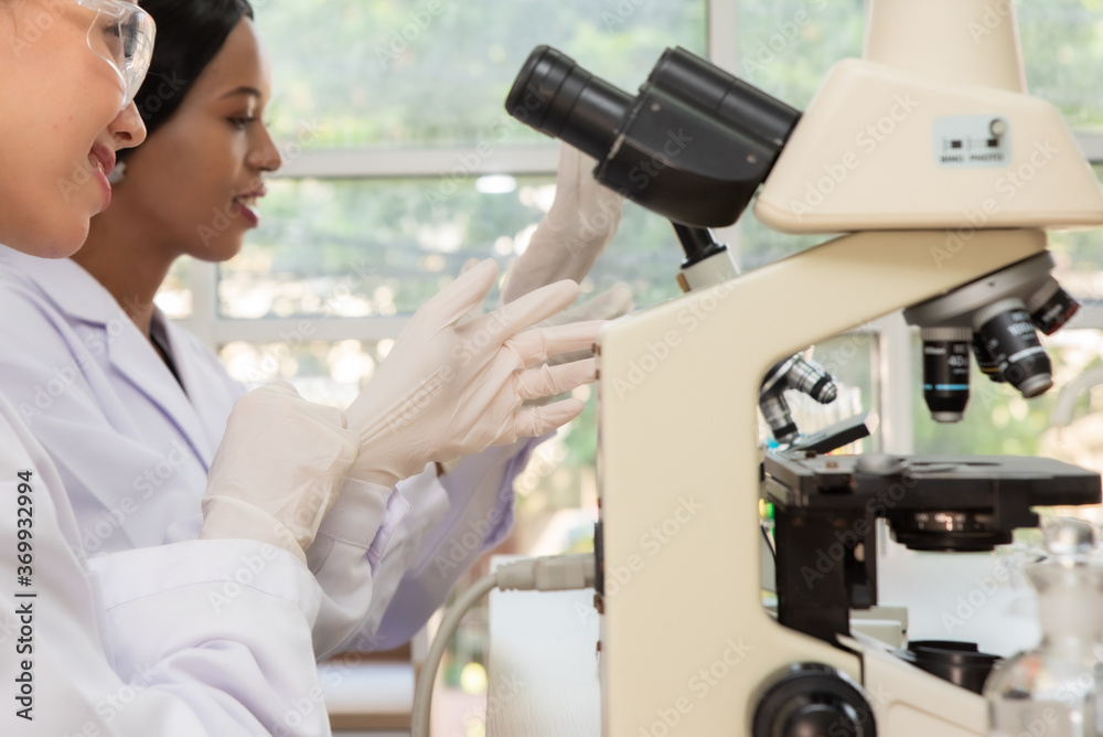 Side View Of Female Scientist With Colleague Wearing Gloves At Laboratory