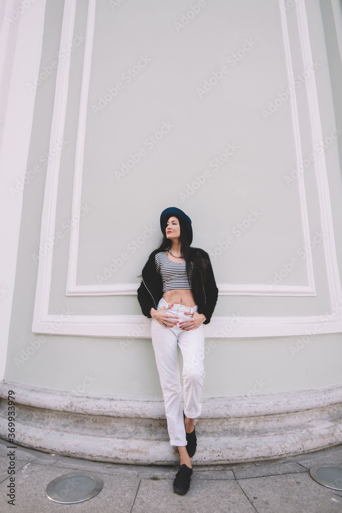 Full length portrait of the young model leaning against vintage wall with copy space area, beautiful and fashionable hipster girl posing near ancient building while dreaming about something special