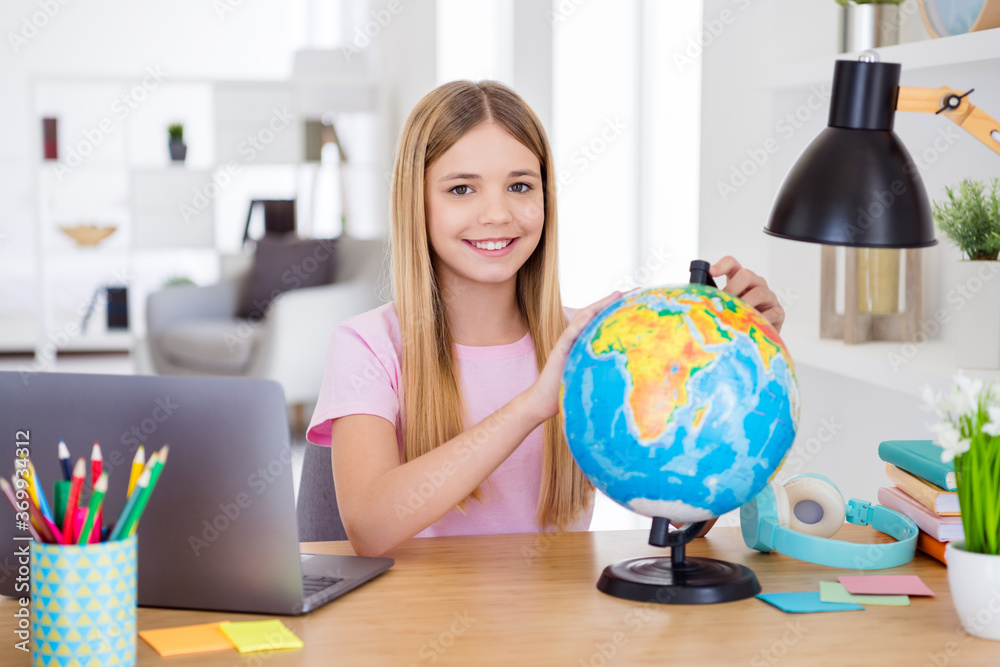 Photo of positive girl child sit table desk study remote use globe want explore earth continent in house indoors Photo of positive girl child sit table desk study remote use globe want explore earth continent in house indoors