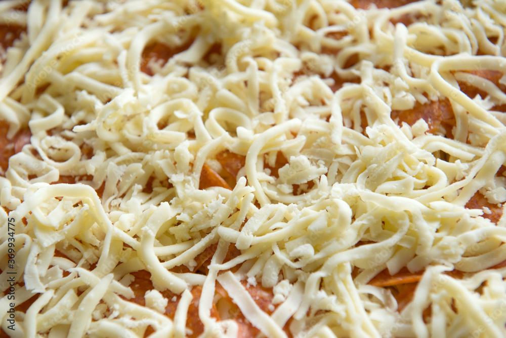 Pieces of pepperoni sausage among grated cheese before baking, close-up. Cooking pizza. Pieces of pepperoni sausage among grated cheese before baking, close-up. Cooking pizza.