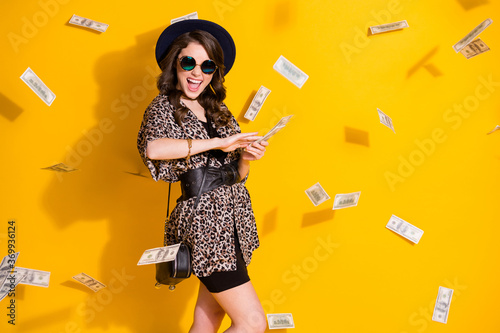 Photo of positive crazy girl spend waste usd cashback credit bank profit air fly money isolated over bright shine color background wear headwear skirt sunglass clutch