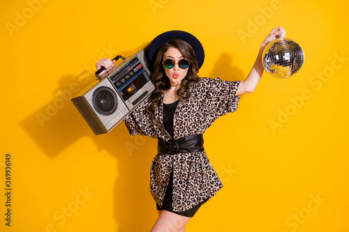 Photo of dreamy cute girl hold glitter ball play record rhythm cassette boom box send air kiss wear skirt headwear sunglass isolated over yellow color background