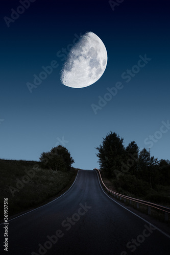 A road leading toward huge and beautiful moon on night sky