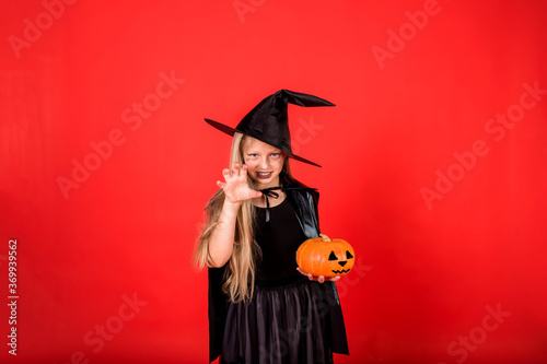 Funny girl witch in a hat with a pumpkin on a red isolated background with space for text