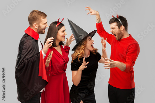 friendship, holiday and people concept - group of happy smiling friends in halloween costumes of vampire, devil, witch and cheetah scaring each other over grey background photo
