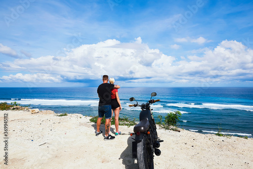 Romantic couple enjoying beautiful scenery of ocean stopping during journey traveling by motorbike, back view of lovers hugging on cost of sea fascinated with natural landscape and skyline on summer .