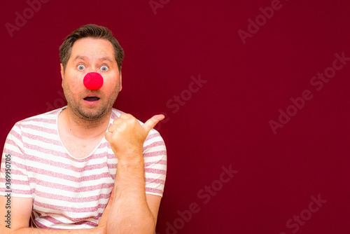 The happy surprised charming trendy and smiling man on red nose day or april fools day.Man shows to the side