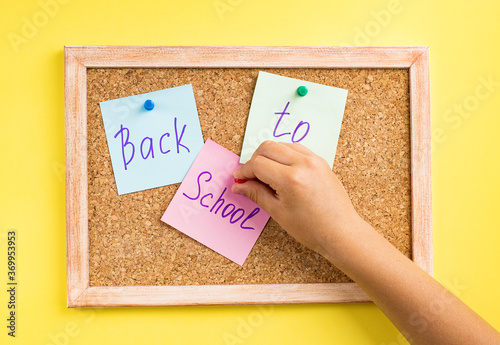 A child's hand attaches colored notes to a cork Board. Yellow background. Let's go back to the concept of the school. Flatley