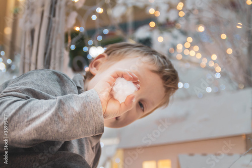 A blond European boy wants to throw a snowball made of artificial snow. New year and Christmas decorations.