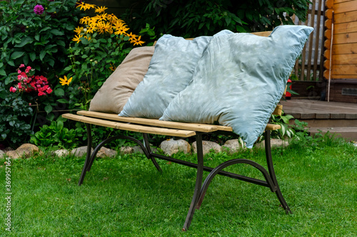 Three old pillows without pillowcases dry on a bench in the garden among green grass and a flower bed.