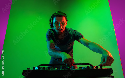 Fire. Young caucasian musician in headphones performing on bicolored pink-purple background in neon light. Concept of music, hobby, festival. Joyful party host, DJ. Colorful portrait of artist.