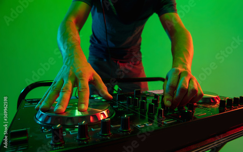 Close up young musician in headphones performing on green background in neon light. Concept of music, hobby, festival, entertainment, emotions. Joyful party host, DJ. Colorful portrait of artist.