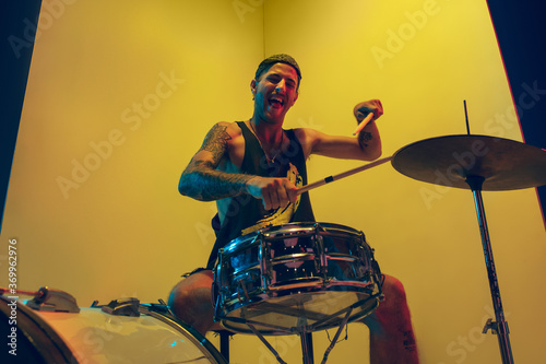 Emotional. Young musician with drums performing on yellow background in neon light. Concept of music, hobby, festival, entertainment, emotions. Joyful, inspired drummer. Colorful portrait of artist. photo